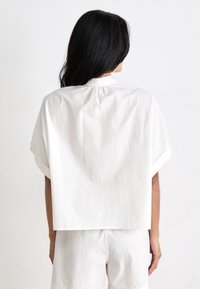 Corto top bianco a maniche corte, a forma boxy con scollatura rotonda e dettaglio arricciato sul retro. Realizzato in tessuto leggero con una finitura leggermente testurizzata.