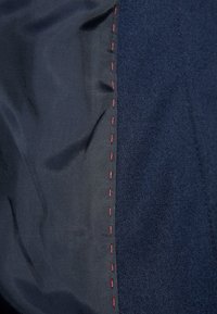 Gros plan sur un tissu bleu marine foncé avec des coutures rouges verticales faites à la main le long de la couture entre les sections textiles lisses et texturées.