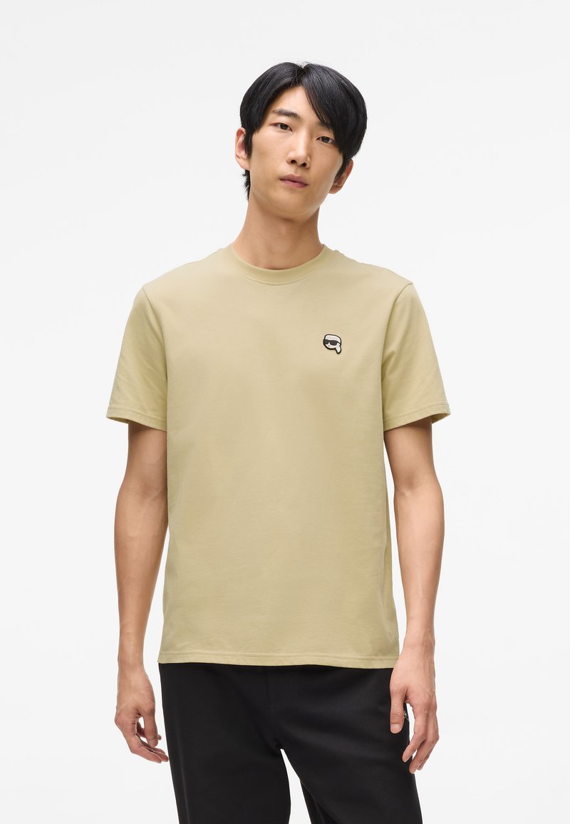 Khaki bavlnené tričko s okrúhlym výstrihom a krátkymi rukávmi. Má malé čierno-biele logo na ľavej strane hrude. Priamy strih.