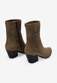 Botas de tobillo de ante marrón con cierre de cremallera, punta cuadrada y un tacón bajo y grueso, que cuentan con tachuelas plateadas en la parte frontal.