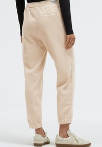 Helle beige gemusterte Jogger-Hosen mit einem elastischen Bund und Knöchelbündchen, aus strukturiertem Stoff gefertigt. Getragen mit hellen Sneakers.