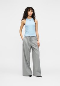 Ανοιχτό μπλε αμάνικο τοπ με ριμπ ύφανση, συνδυασμένο με φαρδιά γκρι παντελόνια με κορδόνι στη μέση, ολοκληρωμένο με μαύρα παπούτσια με τακούνι.