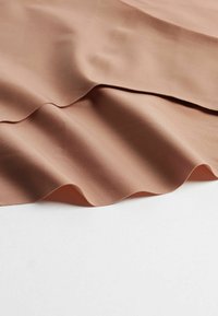 Ljusbrunt tyg med en slät yta, som har mjuka vågor och veck. Materialet verkar mjukt med en subtil lyster.