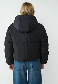 Czarna krótka kurtka puchowa z kapturem, o gładkiej fakturze i widocznych szwach. W połączeniu z dżinsami w kolorze niebieskim z wysokim stanem.