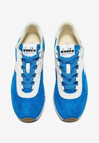 Sneaker blu in suede con accenti bianchi in pelle, dotate di lacci blu, punta arrotondata e suola in gomma testurizzata. Marchio Diadora Heritage visibile.