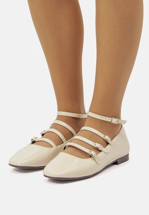 Ballerines en cuir verni beige avec un bout pointu, dotées de plusieurs sangles ajustables sur le cou-de-pied et la cheville. Semelle plate avec un matériel minimal.