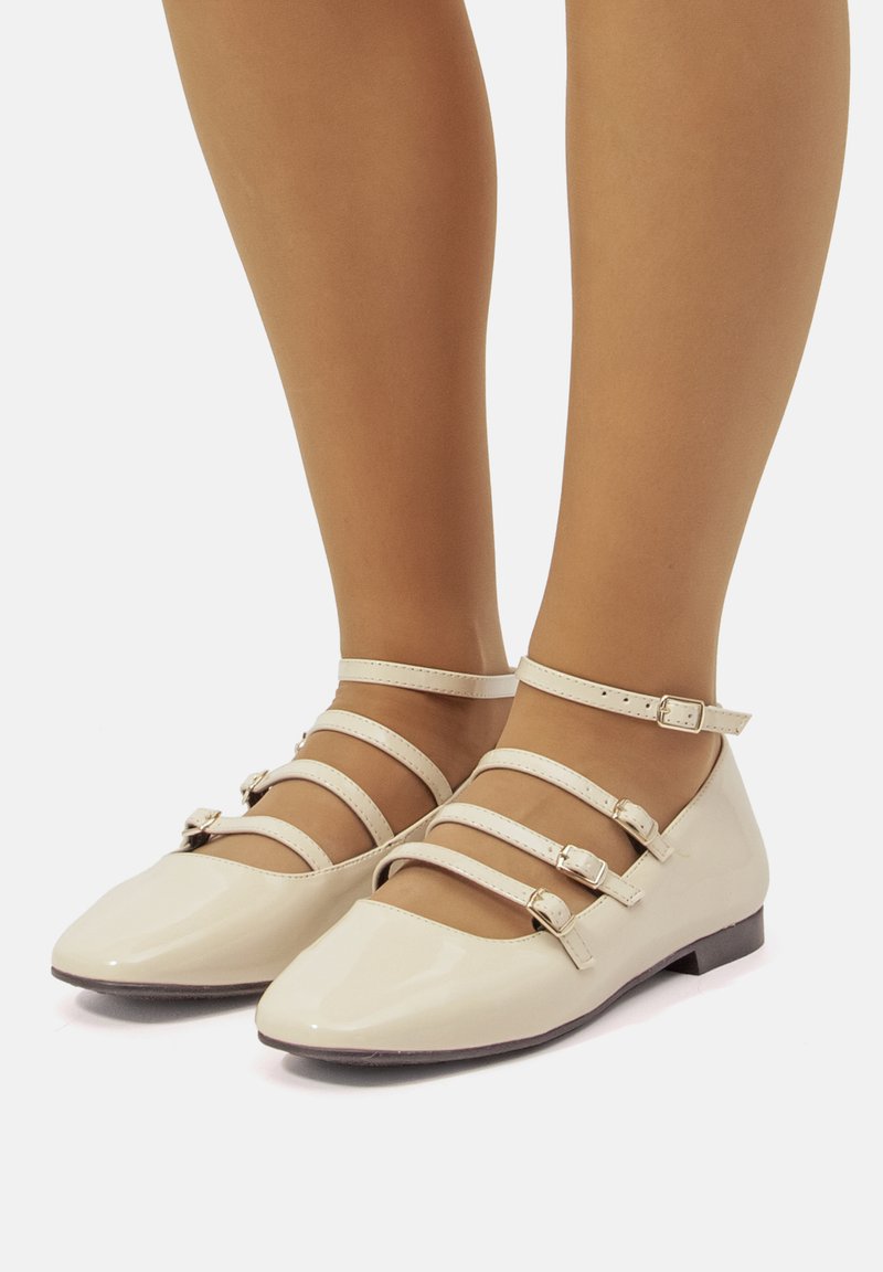 Ballerines en cuir verni beige avec un bout pointu, dotées de plusieurs sangles ajustables sur le cou-de-pied et la cheville. Semelle plate avec un matériel minimal.