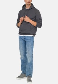 Gray cotton hoodie with a front pocket and adjustable drawstring hood, paired with light blue denim jeans and gray sneakers.