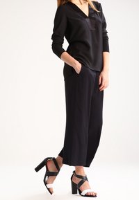 Blusa nera a maniche lunghe con scollatura a V e texture satinata, abbinata a pantaloni neri a gamba larga e sandali con tacco alta con strisce bianche e nere.