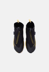 Ζευγάρι μαύρα και κίτρινα αδιάβροχα αθλητικά παπούτσια ψηλού τύπου με κλειδώματα με διακόπτη και θηλιές έλξης, σε θέα από πάνω σε λευκό φόντο.