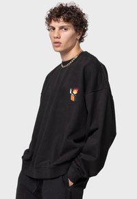 Sudadera negra de gran tamaño hecha de algodón, con un cuello redondo y hombros caídos. Presenta un gráfico en el pecho de un encendedor y llamas.