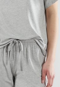 Sivi pamukasti loungewear s remenom u struku i opuštenim krojem. Meki, lagani materijal s kratkim rukavima i bočnim džepovima.