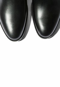 Zapatos de vestir de cuero negro con un acabado suave, punta redonda y un sutil detalle de costura a lo largo de los bordes. La forma de la suela es elegante y aerodinámica.