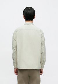 Világosszürke, hosszú ujjú ing texturált anyagból, gallérral és gombos mandzsetta részletekkel. Minimalista kialakítás, laza szabással.