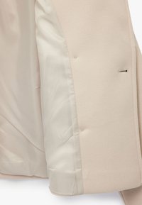 Beige uldblandingsfrakke med glat satinfor. Har en notched krave, subtil tekstur og to diskrete knapper på ydersiden.