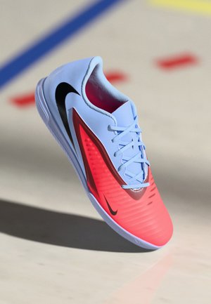 Nike sportieve schoen met een lichtblauwe bovenkant, rode accenten, een gestructureerd zijpaneel en een zwart swoosh-logo. Voorzien van een vetersysteem en een ronde zool.