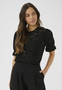 Un haut noir brodé avec des manches bouffantes, des motifs floraux découpés et un tissu texturé, associé à un pantalon taille haute noir.