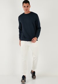 Felpa blu navy con maniche lunghe, scollatura rotonda e polsini a costine. Abbinata a pantaloni jogger color crema, con polsini elasticizzati e tasche.