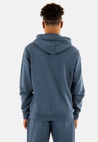 Sudadera con capucha en azul oscuro, con un ajuste relajado, textura suave y puños y dobladillo de canalé. La vista trasera muestra la capucha y la simplicidad del diseño.