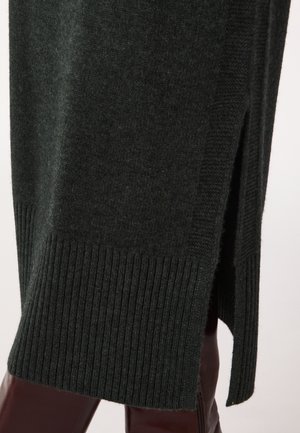Maglione a collo alto di un verde scuro, lavorato a maglia, con orlo a coste e spacchi laterali, che mette in mostra una texture morbida e una silhouette aderente.