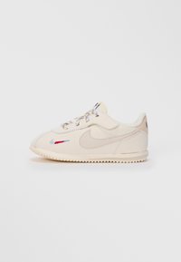 Off-white Nike tenisice s teksturiranom potplatom, izvezeni crveni i plavi pažnju s bočne strane, te šarene vezice na jednostavnoj pozadini.
