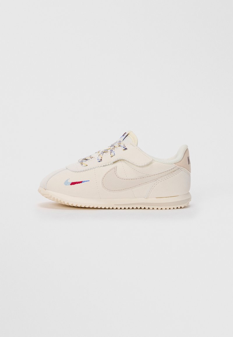 Off-white Nike tenisice s teksturiranom potplatom, izvezeni crveni i plavi pažnju s bočne strane, te šarene vezice na jednostavnoj pozadini.
