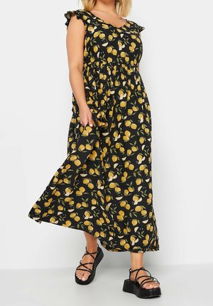 Vestido maxi con fondo negro y un patrón de limones amarillos, mangas con volantes y cintura ceñida. Combinado con sandalias de plataforma negras.