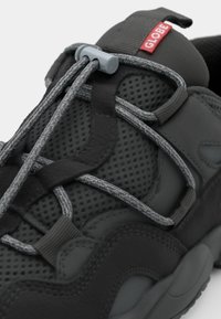 Close-up of a dark gray sneaker with mesh detailing and elastic laces. A red logo labeled "GLOBE" is visible on the tongue.