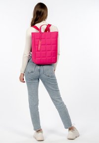 Mochila cuadrada de color rosa brillante, hecha de material texturizado, con un asa en la parte superior y correas de hombro ajustables. Presenta una etiqueta sencilla.