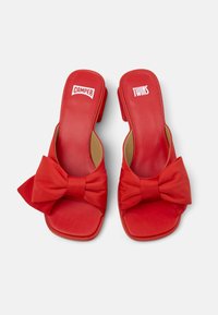 Red slide sandals with a large bow detail, made from smooth material. Square toe and small heel, featuring "CAMPER" and "TWINS" branding.