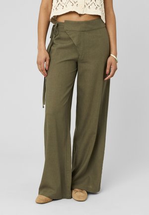 Pantalon large vert olive avec détail à nouer sur le côté gauche, porté avec des ballerines beiges et un haut en crochet crème.