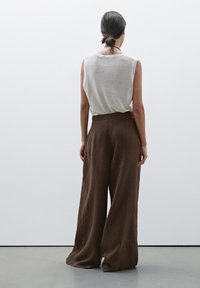 Haut sans manches gris clair associé à un pantalon en lin marron ample et large. Les textures et les coutures visibles renforcent l'apparence structurée du vêtement.