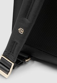 Schwarzer Taschenriemen mit strukturiertem Leder, glattem Stoff und goldfarbenen Beschlägen mit Logodetail. Nahaufnahme betont den Materialkontrast.