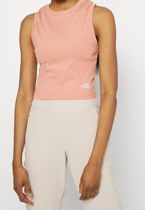 Femme portant un crop top pêche côtelé sans manches avec le logo The North Face et un pantalon beige taille haute avec poches latérales