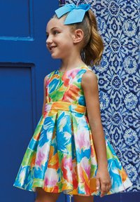 Abito floreale colorato con maniche corte, fiocco blu nei capelli, gonna svasata e tonalità vivaci di rosa, arancione, verde e blu.