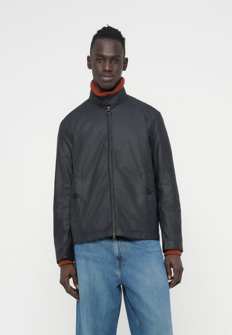 Μαύρο μπουφάν με όρθιο γιακά, κλείσιμο με φερμουάρ και δύο μπροστινές τσέπες, συνδυασμένο με πορτοκαλί ζιβάγκο με ριμπ ύφανση από κάτω.