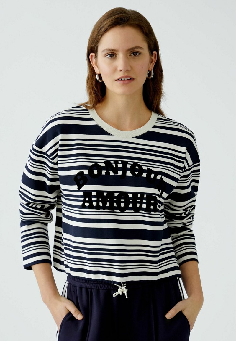 Navy en witte gestreepte sweatshirt met lange mouwen, voorzien van de tekst "BONJOUR AMOUR" in vetgedrukte zwarte letters. Van katoenmix materiaal.