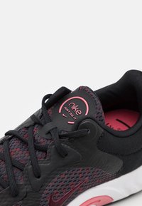 Scarpe sportive in maglia nera con dettagli testurizzati, accenti rosa e lacci neri. Presentano una linguetta con logo rotondo e un collare alla caviglia imbottito.