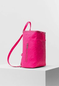 Sac à dos rectangulaire rose vif avec nom de marque en relief, fermeture éclair supérieure, poche avant verticale zippée, et bretelles réglables.