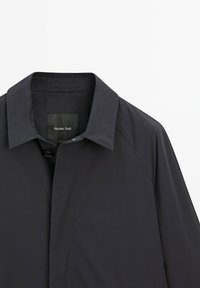 Giacca nera leggera con colletto classico e chiusura a bottoni. Tessuto liscio con maniche raglan e design minimalista. Etichetta del marchio visibile.