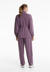 Lilla loungewear sæt med en taljeret top med høj krave og lange ærmer, parret med løstsiddende bukser. Blød stoftekstur.