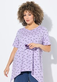 Lilla v-hals t-shirt med sort palmetræ-tryk, korte ærmer og ujævnt fald. Modellen holder en lilla accessory. Stoffet ser blødt og åndbart ud.