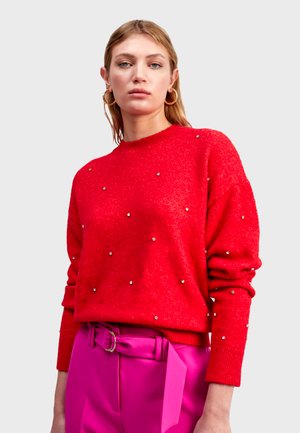 Rode trui met een zachte textuur, versierd met zilveren studs, met een ronde hals en lange mouwen, gecombineerd met hooggeplaatste roze broeken.