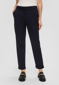 Marineblaue, maßgeschneiderte Hose mit geradem Bein, umgeschlagenen Säumen und Seitentaschen, kombiniert mit schwarzen Mokassins mit goldenen Hardware-Details.