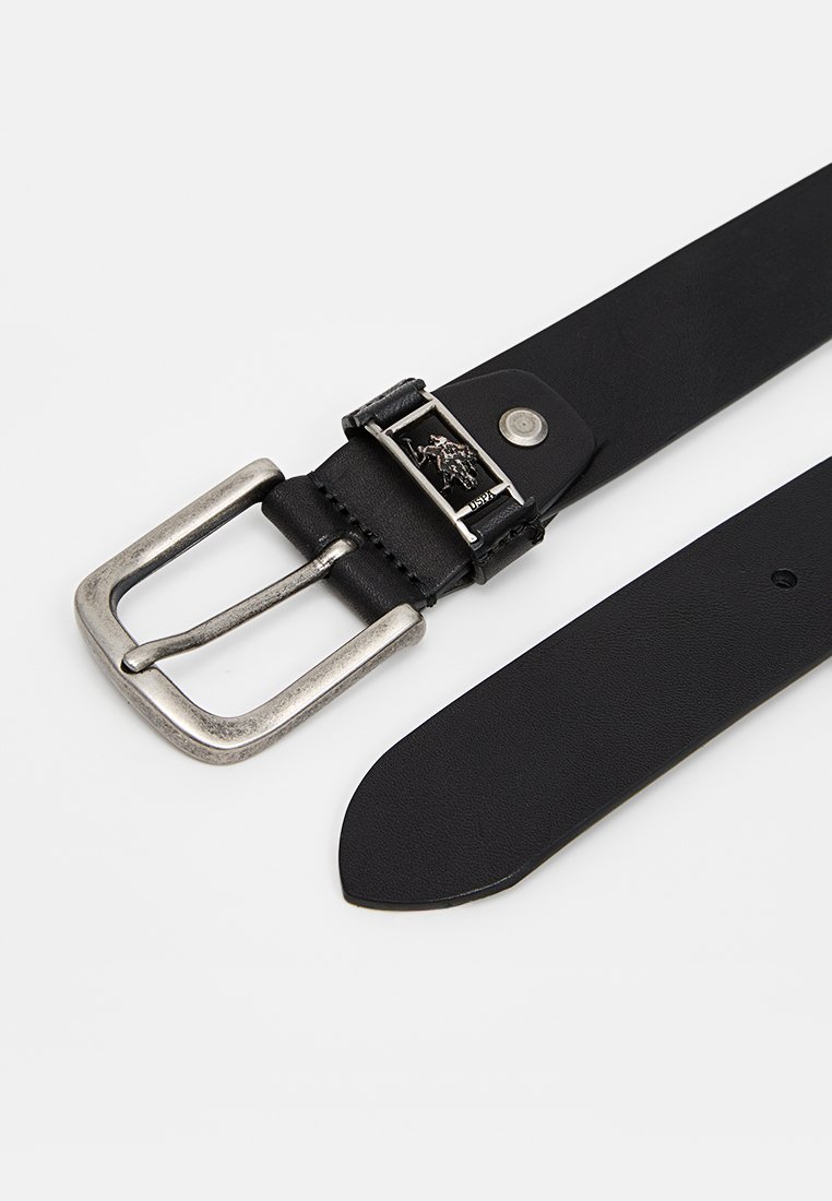 Zwarte leren riem met een zilveren gesp. De gesp heeft een logo en een pinmechanisme. De riem heeft een soepele textuur en een taps toelopende punt.