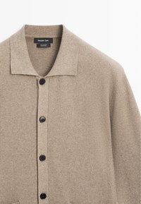 Cardigan beige in maglia a coste con bottoni neri, colletto aperto e etichetta Massimo Dutti su tessuto di cotone.