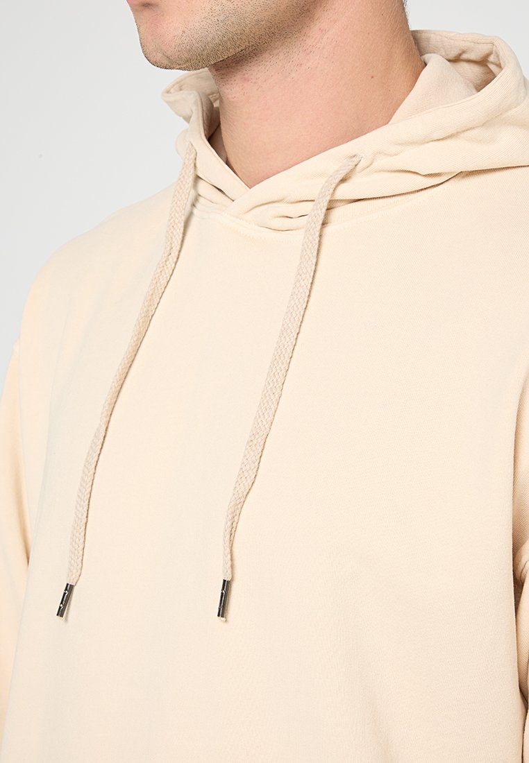 Felpa beige con cappuccio regolabile, realizzata in tessuto testurizzato e con estremità del cordino in argento. Design semplice senza motivi o accenti.