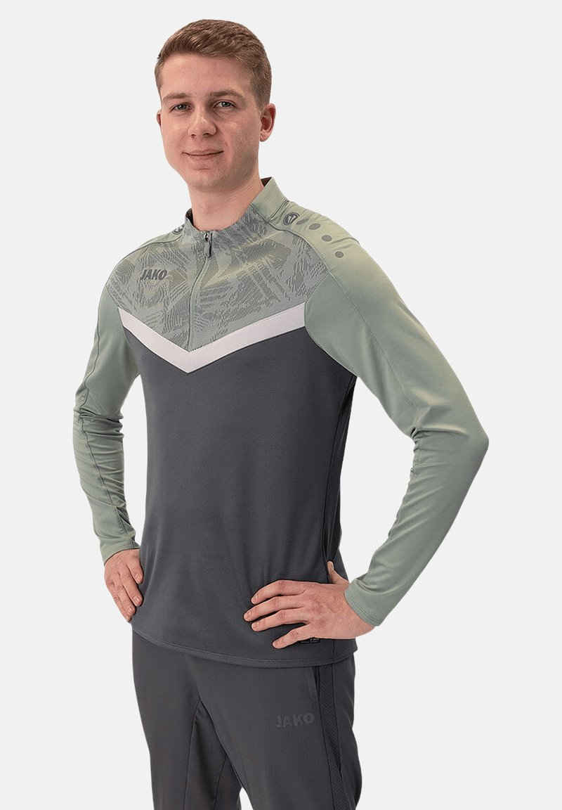 Maglietta atletica grigio e verde a maniche lunghe con mezza zip, caratterizzata da un design a chevron bianco, parte superiore testurizzata e accenti sulle spalle.