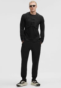 Conjunto atlético negro que incluye una camiseta de manga larga con un acabado texturizado, un chaleco exterior con tirantes ajustables y joggers ajustados.