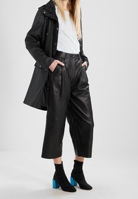 Sort vandtæt jakke over en lyseblå skjorte, kombineret med højtaljede læder culotter og ankelstøvler med blå blokhæl.